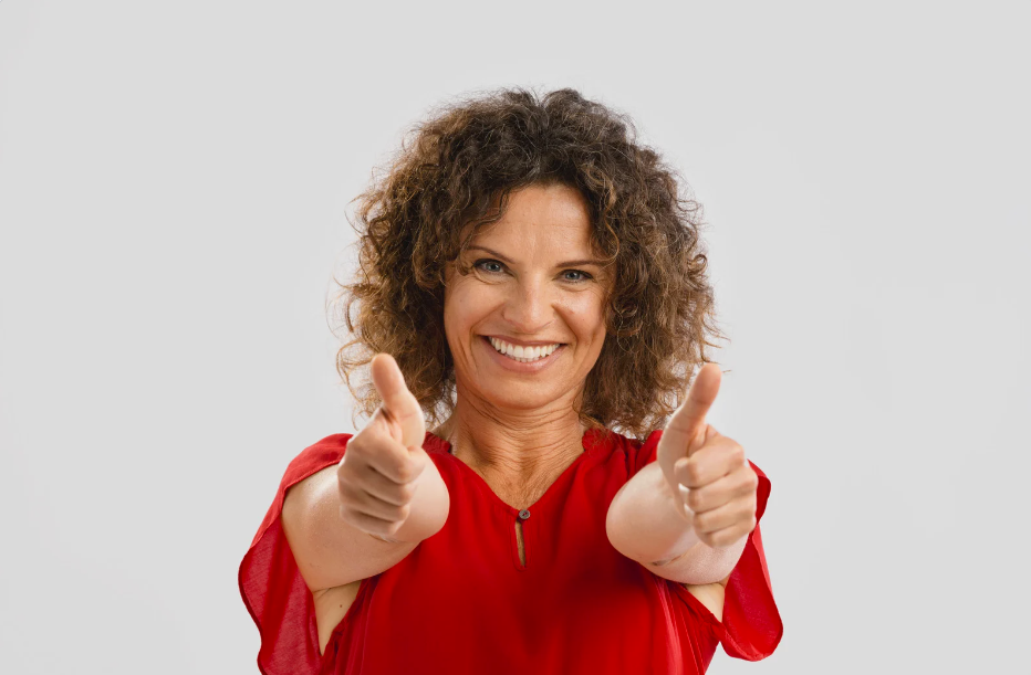 Woman in a red blouse smiling with both thumbs raised.