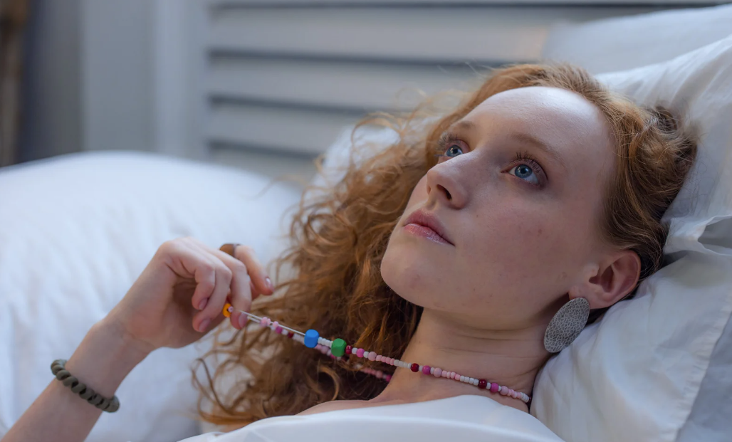 Person lying on pillows and holding a colourful beaded necklace.