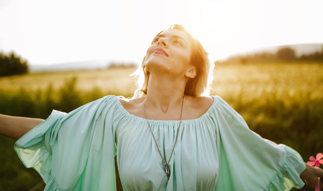 Person in a pale mint blouse looking upward in a sunlit field.